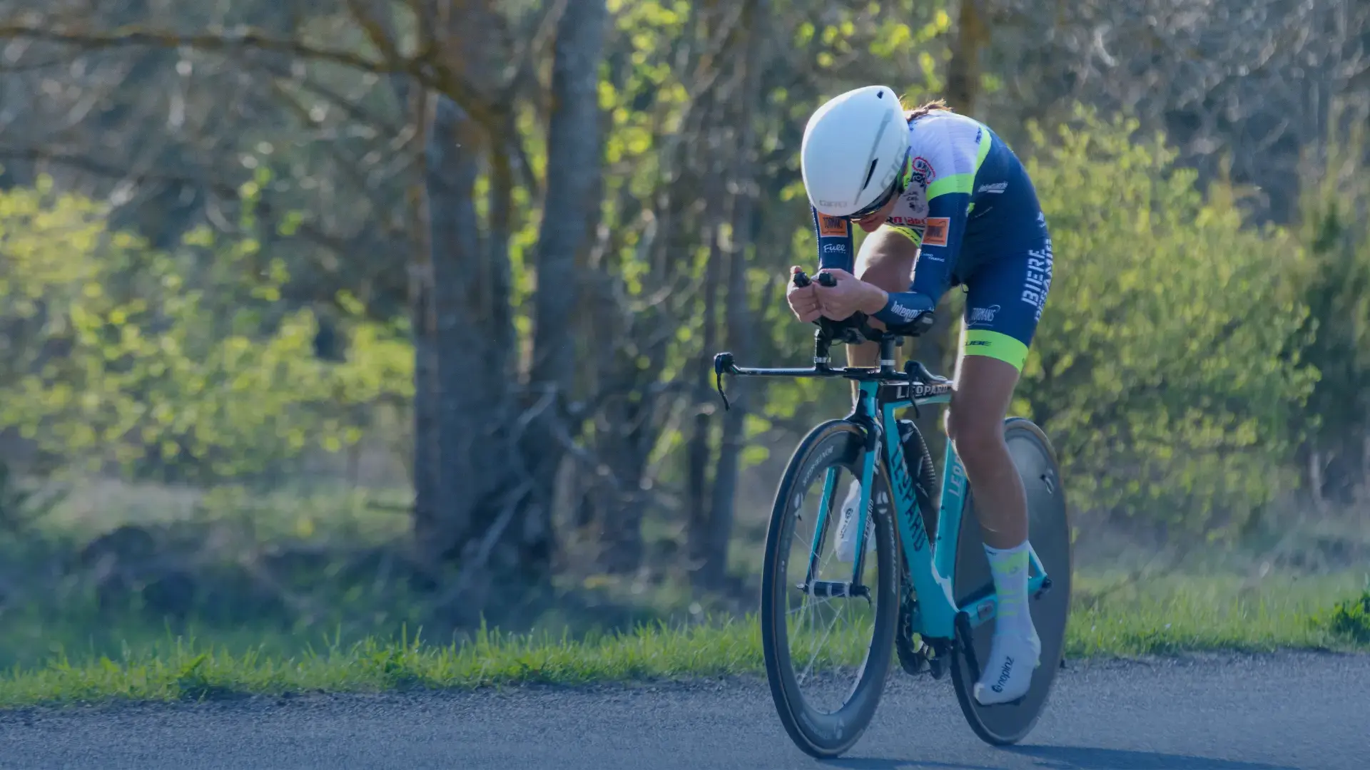 Ciclista profesional compitiendo en carretera con bicicleta de contrarreloj y casco aerodinámico.